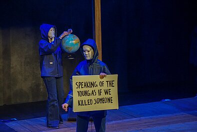 Masked people on stage holding globe and sign.